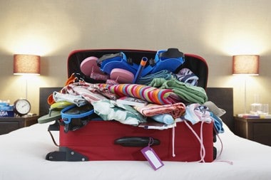 Suitcase overflowing with clothes on a bed