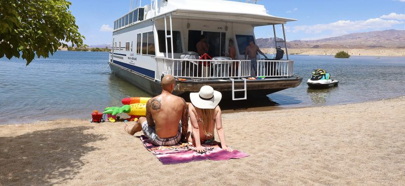 A couple sitting on the beach by a houseboat